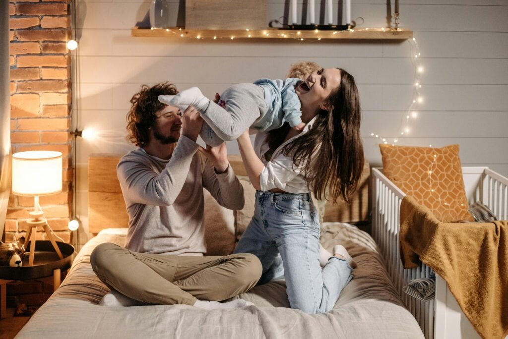 Joyful parents playing with their child on a bed in a warmly lit bedroom.